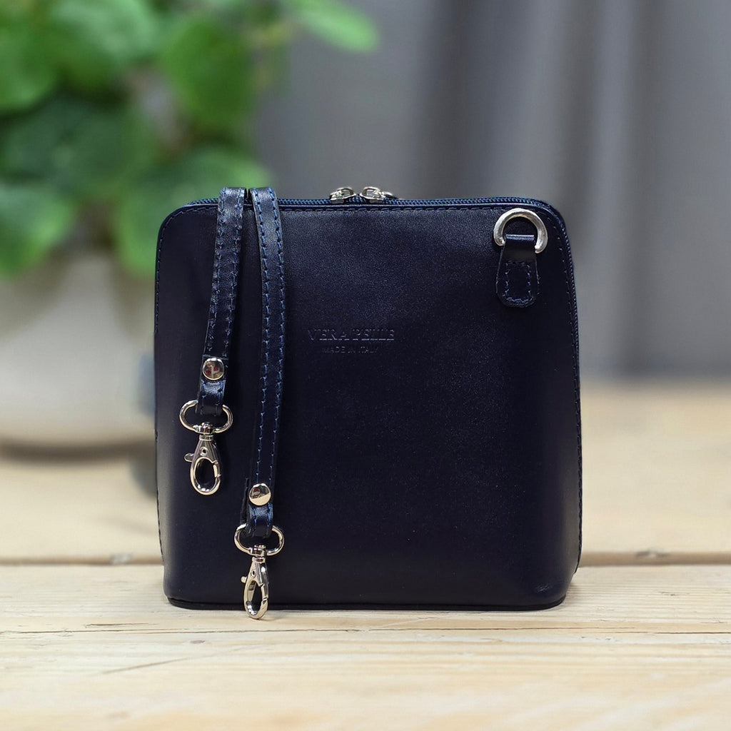 Navy blue leather bag with a strap on a wooden surface