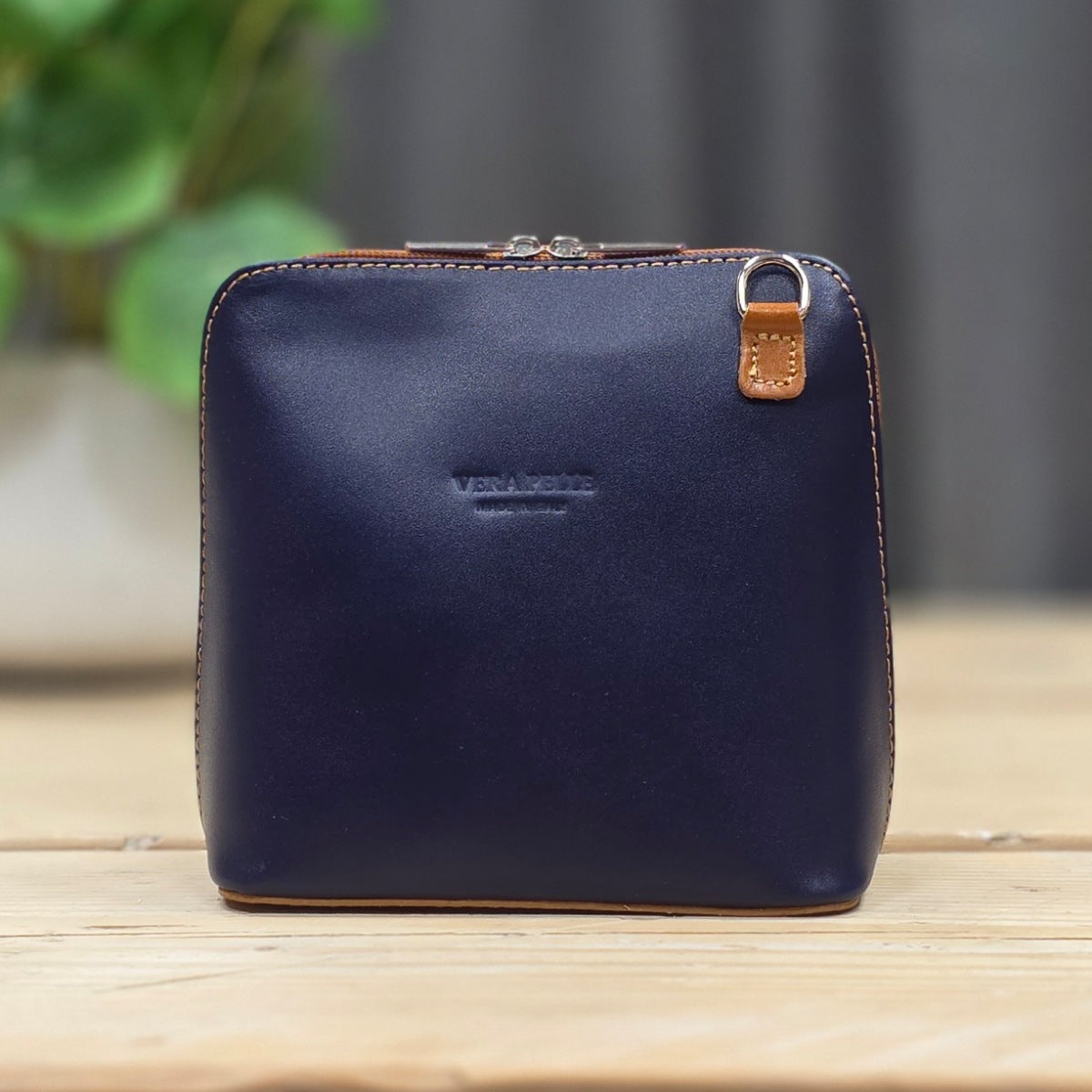 Navy blue leather handbag with brown zipper on a wooden surface