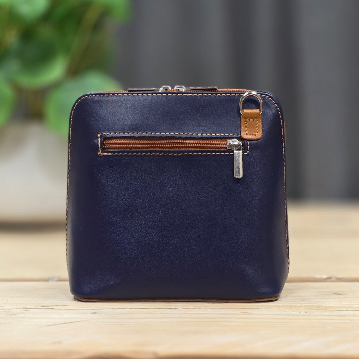 Blue leather handbag with brown zipper on a wooden surface