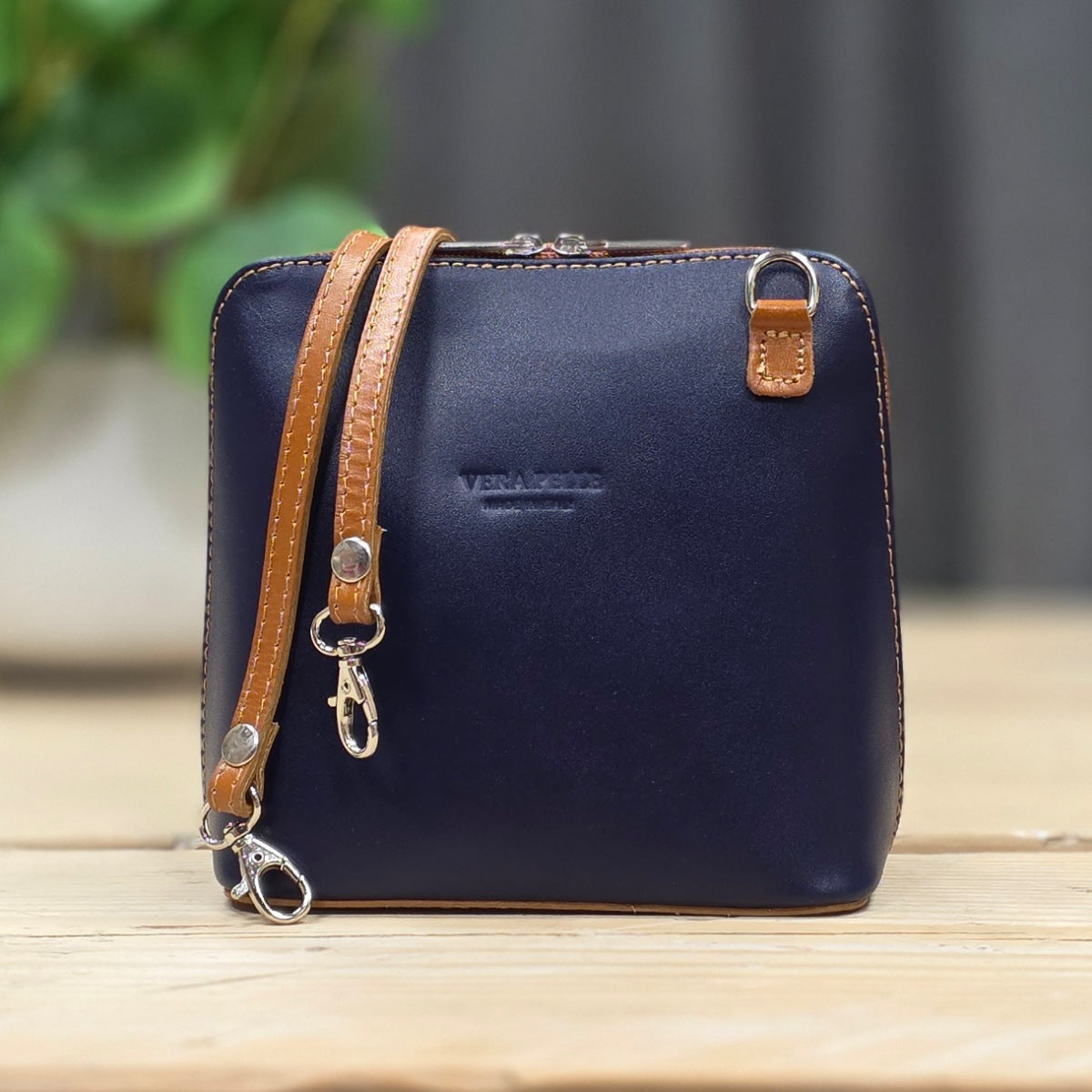 A navy blue leather handbag with tan leather strap and trim, featuring silver-tone hardware set on a light wooden surface.