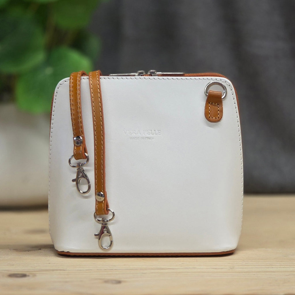 White handbag with brown strap on a wooden surface