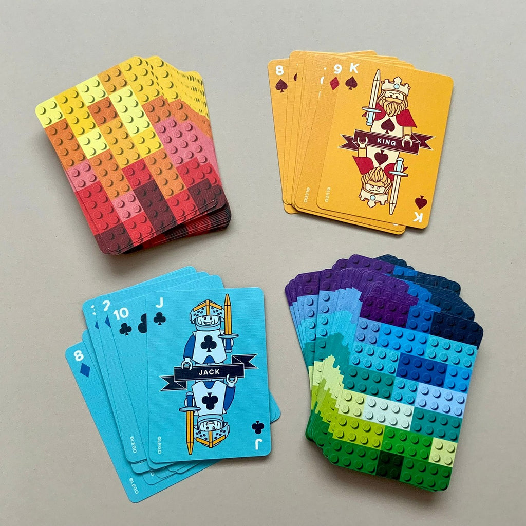 Four decks of building-block-style playing cards arranged on a light beige surface. Two decks are fanned out to show colorful stud tops, and two decks are face-up showing illustrated Jack, 8, 9, and 10 cards.