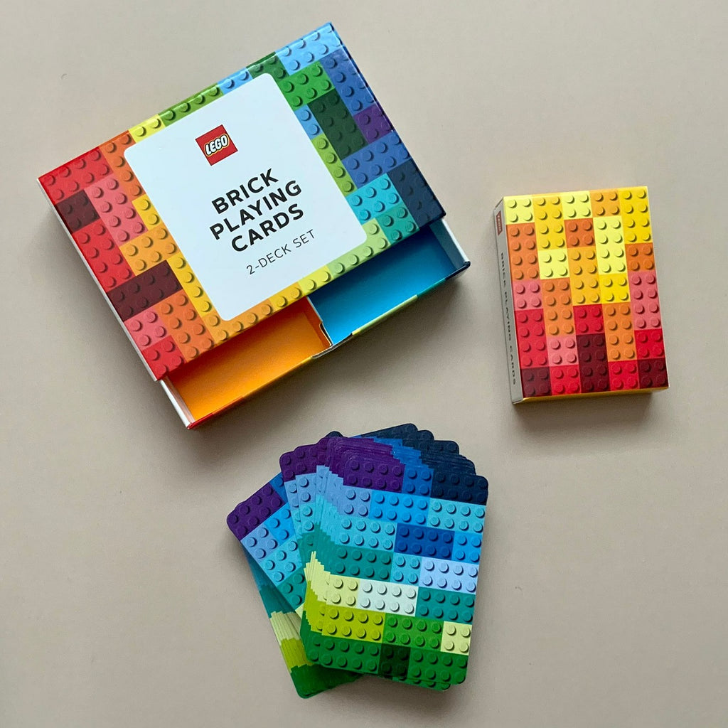 A LEGO Brick Playing Cards 2-Deck Set shown with its open box, a smaller closed box, and a fan of playing cards on a plain beige surface.