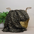 A dark olive green scarf with a leopard print pattern and a textured gold side pocket, styled next to a green potted plant against a neutral background.