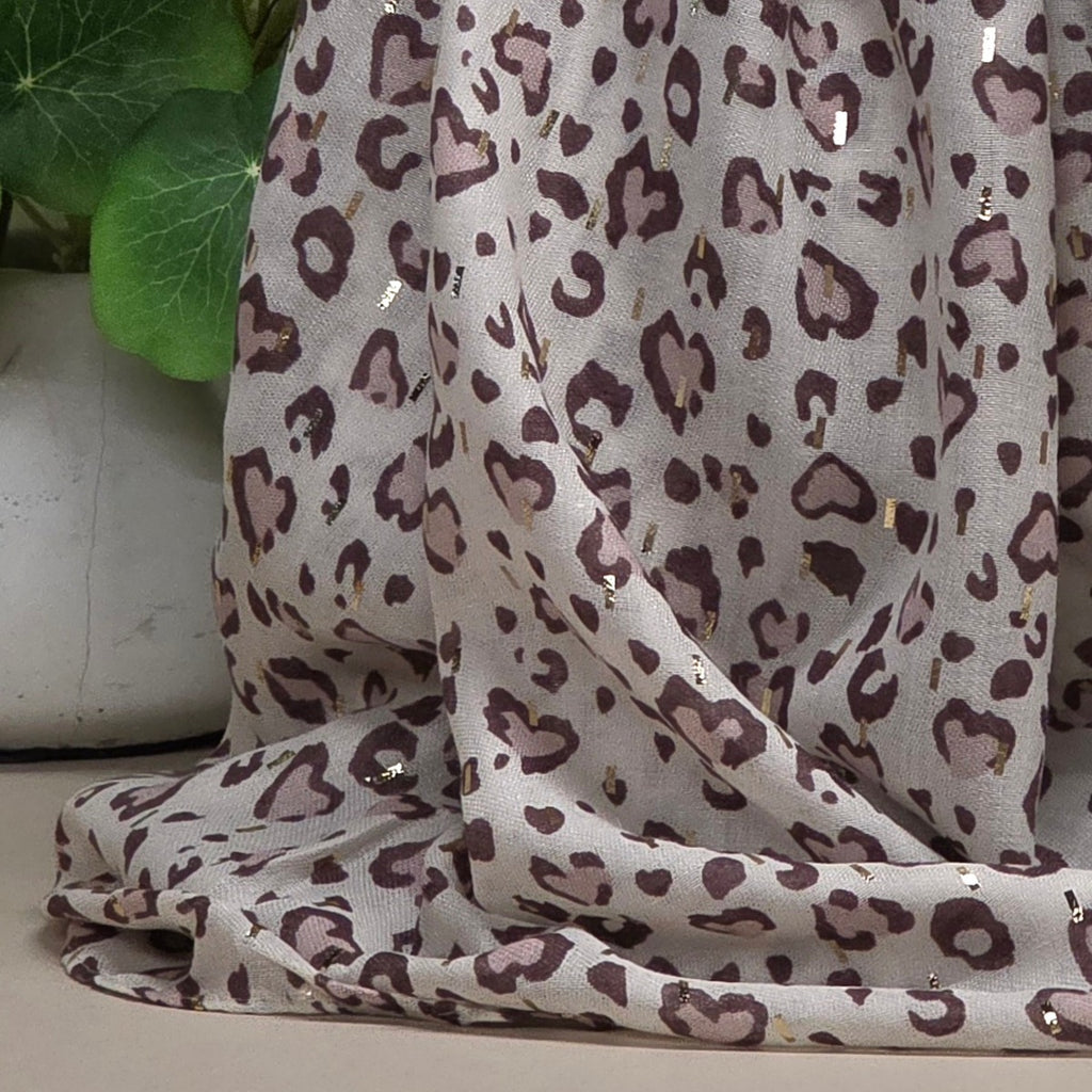 A draped scarf with an all-over leopard print pattern in brown and dusty pink on a light beige background, decorated with small metallic gold sequins.