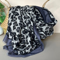 A draped scarf with a grey, black, and dark grey leopard print pattern, featuring a contrasting black and dark grey border, styled in a basket.