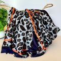A draped scarf with a grey, black, and brown leopard print pattern, featuring a contrasting orange and navy border, styled in a basket.