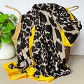 Leopard print black and beige scarf with yellow trim draped over a woven basket on a light surface.
