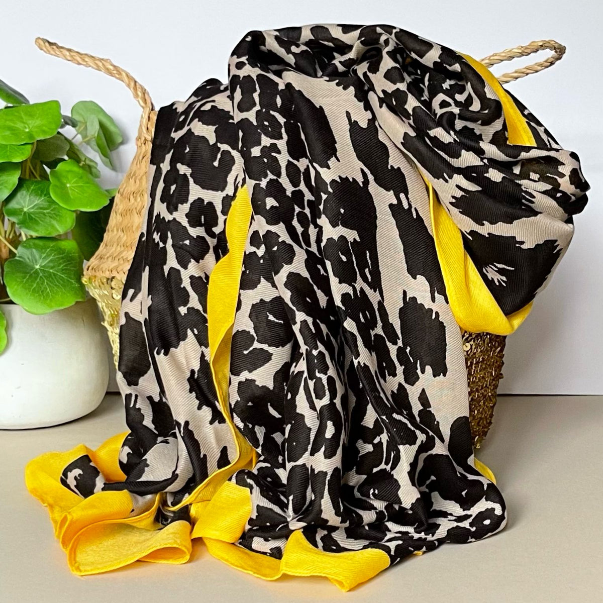 Leopard print black and beige scarf with yellow trim draped over a woven basket on a light surface.