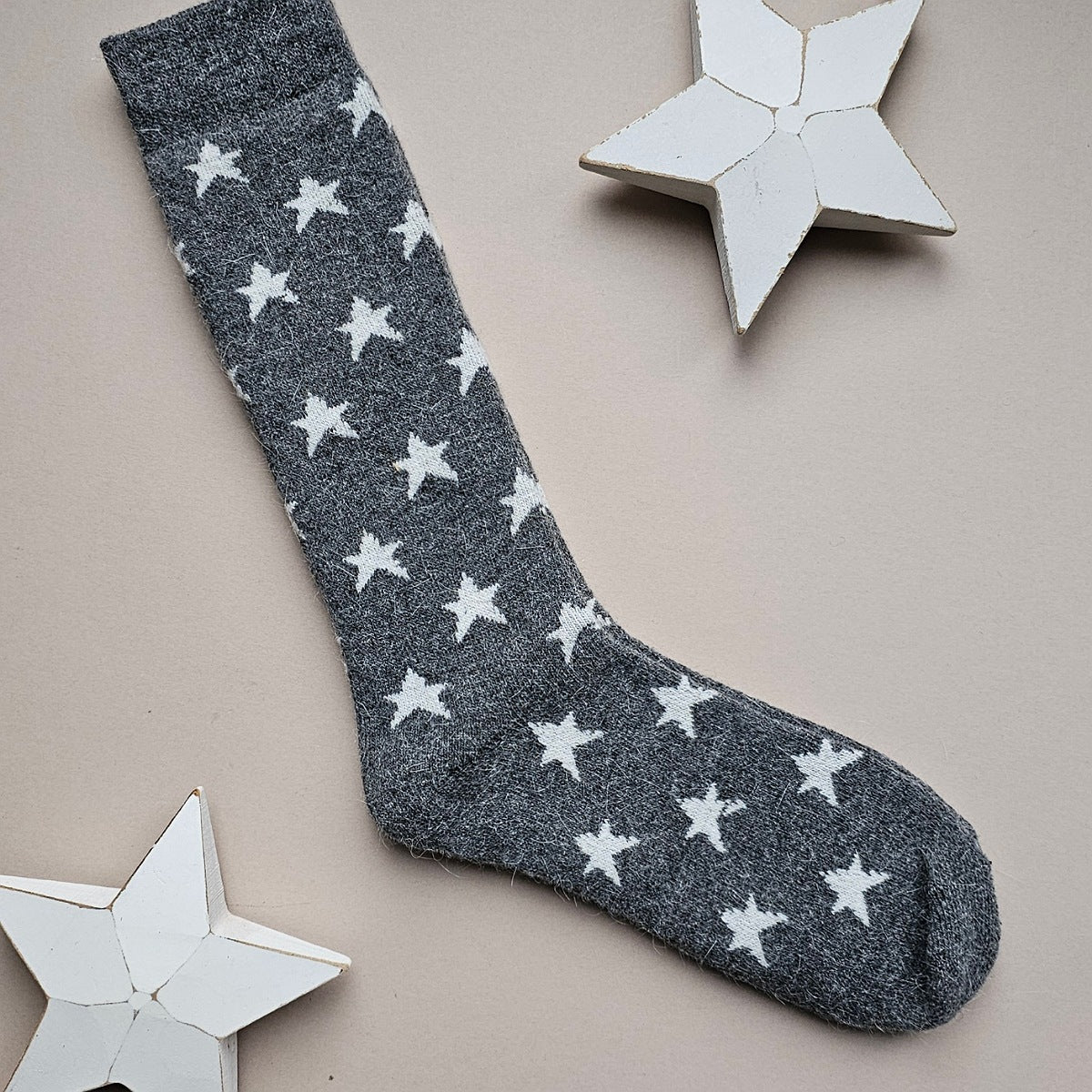 A single dark grey sock with an all-over pattern of white stars, laid flat on a light beige background with decorative white star cutouts.