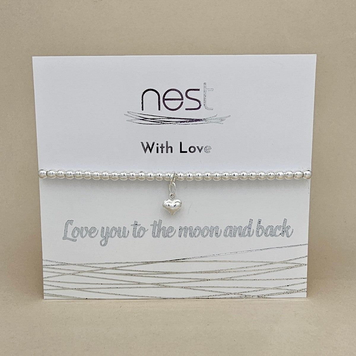 A silver beaded bracelet with a small heart charm, displayed on a white card from the brand 'nest' that reads 'With Love' and 'Love you to the moon and back'.