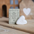 A small white ceramic heart with paw print figurine stands beside its light grey packaging box on a wooden surface. The box is printed with the words 'Best friends leave paw prints on our hearts' and a black heart.