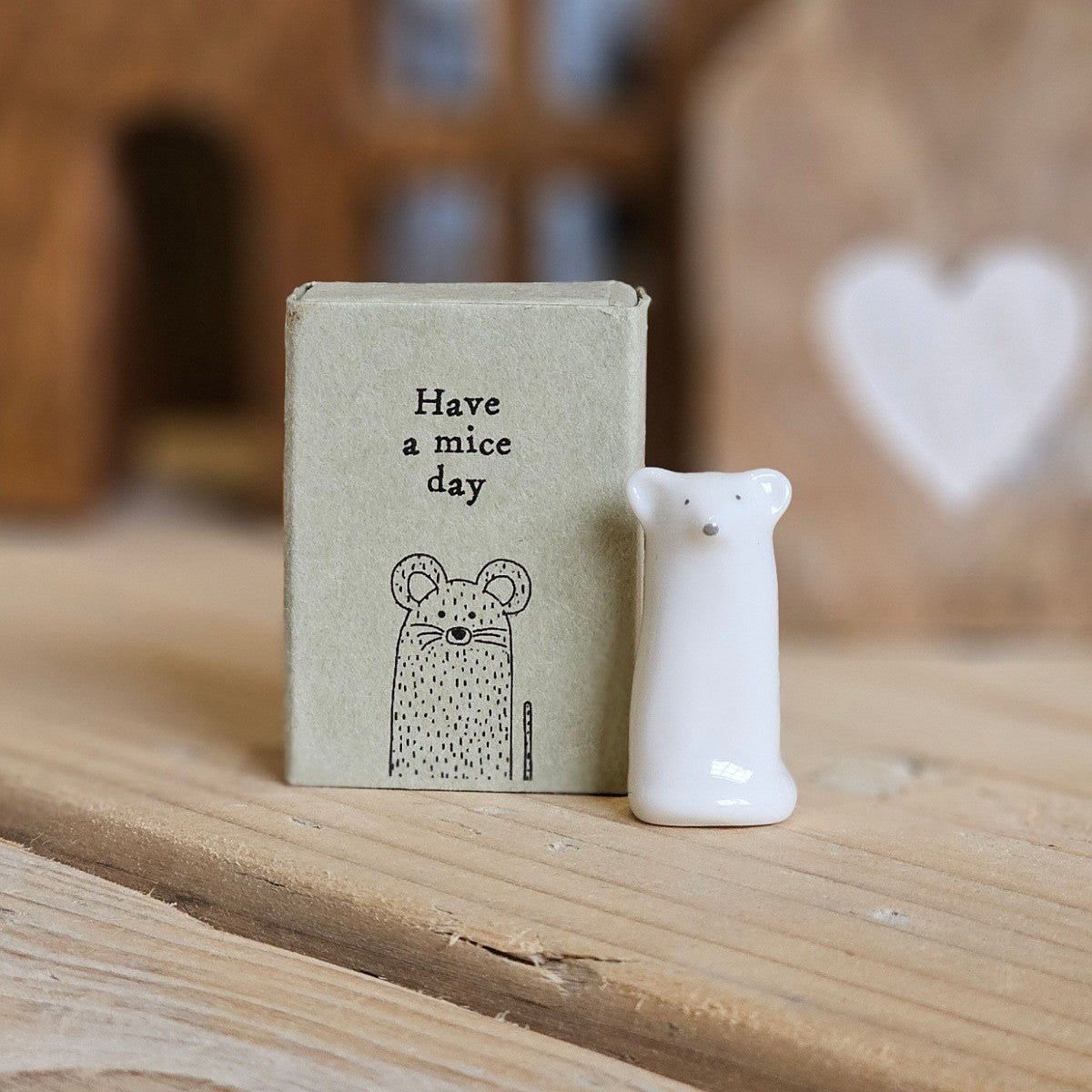 A small white ceramic tall mouse figurine stands beside its light grey packaging box on a wooden surface. The box is printed with the words 'Have a mice day' and a black mouse.