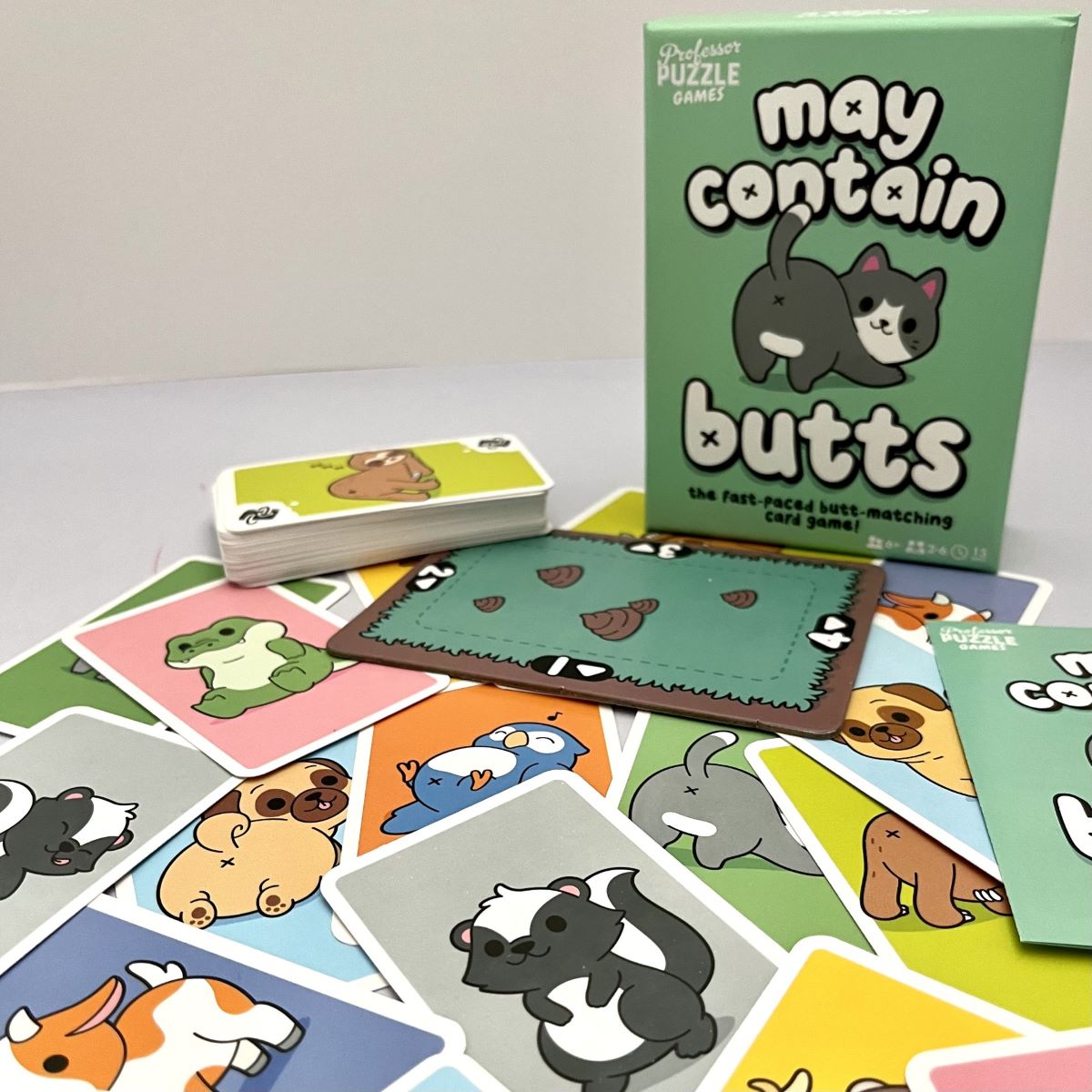 Card game 'may contain butts' with cards and packaging on a light surface