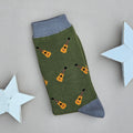 A single green sock with an all-over pattern of yellow and brown acoustic guitars.  Grey ribbed cuffs and heels, styled on a light beige surface with white star props.
