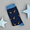 A single navy blue sock with an all-over pattern of yellow and brown acoustic guitars.  Blue ribbed cuffs and heels, styled on a light beige surface with white star props.
