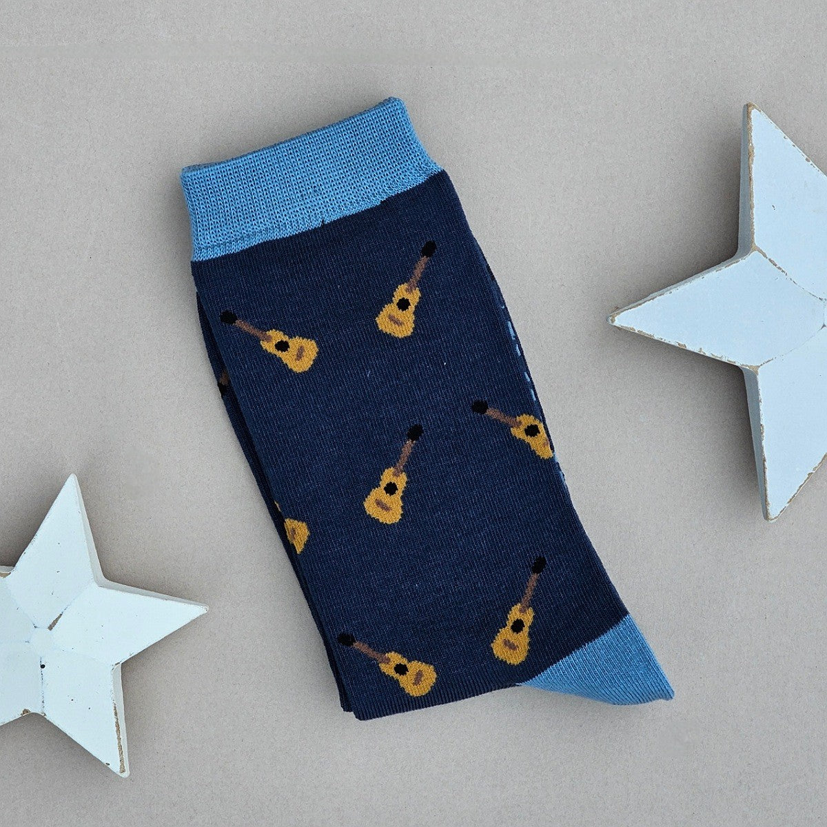 A single navy blue sock with an all-over pattern of yellow and brown acoustic guitars.  Blue ribbed cuffs and heels, styled on a light beige surface with white star props.
