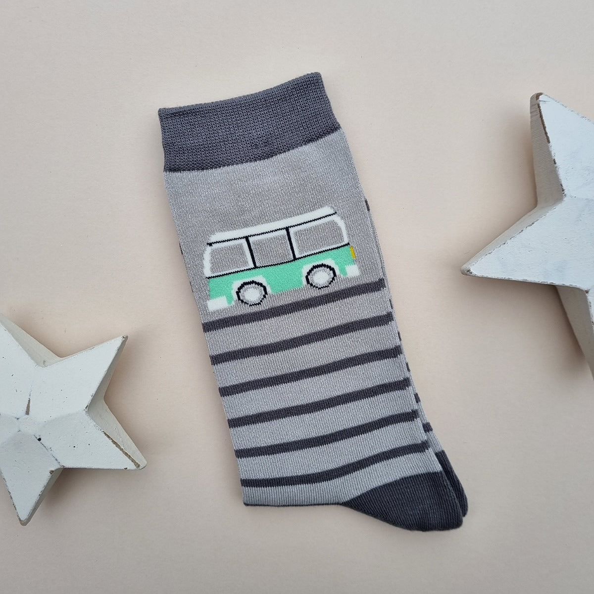 A single silver grey sock featuring a mint green camper van, with various dark grey horizontal stripes.  Dark grey cuff and heel, laid flat on a light beige background with two white star decorations.