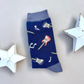 A single navy blue sock with an all-over pattern of blue and red guitars with music notes.  Blue ribbed cuffs and heels, styled on a light grey surface with white star props.
