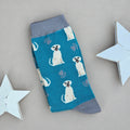 A single blue sock with an all-over  pattern of smiling labradors, with grey printed paws.  Silver grey ribbed cuffs and heels, styled on a light grey surface with white star props.
