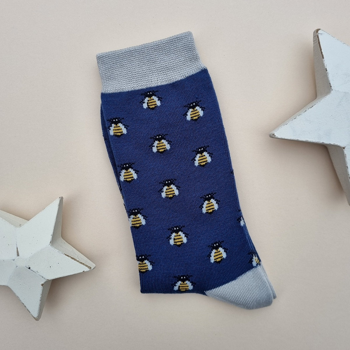 Navy blue sock with honey bee all-over pattern and silver grey cuffs and heel on a light surface with two white star decorations