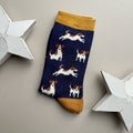 A single navy sock with an all-over pattern of various white and brown jack Russell dogs.  Mustard cuff and heel, displayed on a neutral beige background with white star-shaped props.