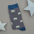 A single grey sock with light grey elephant silhouettes and teal cuff, heel, and toe, laid flat on a light beige background with two white star decorations.