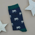 A single navy sock with grey elephant silhouettes and teal cuff, heel, and toe, laid flat on a light beige background with two white star decorations.