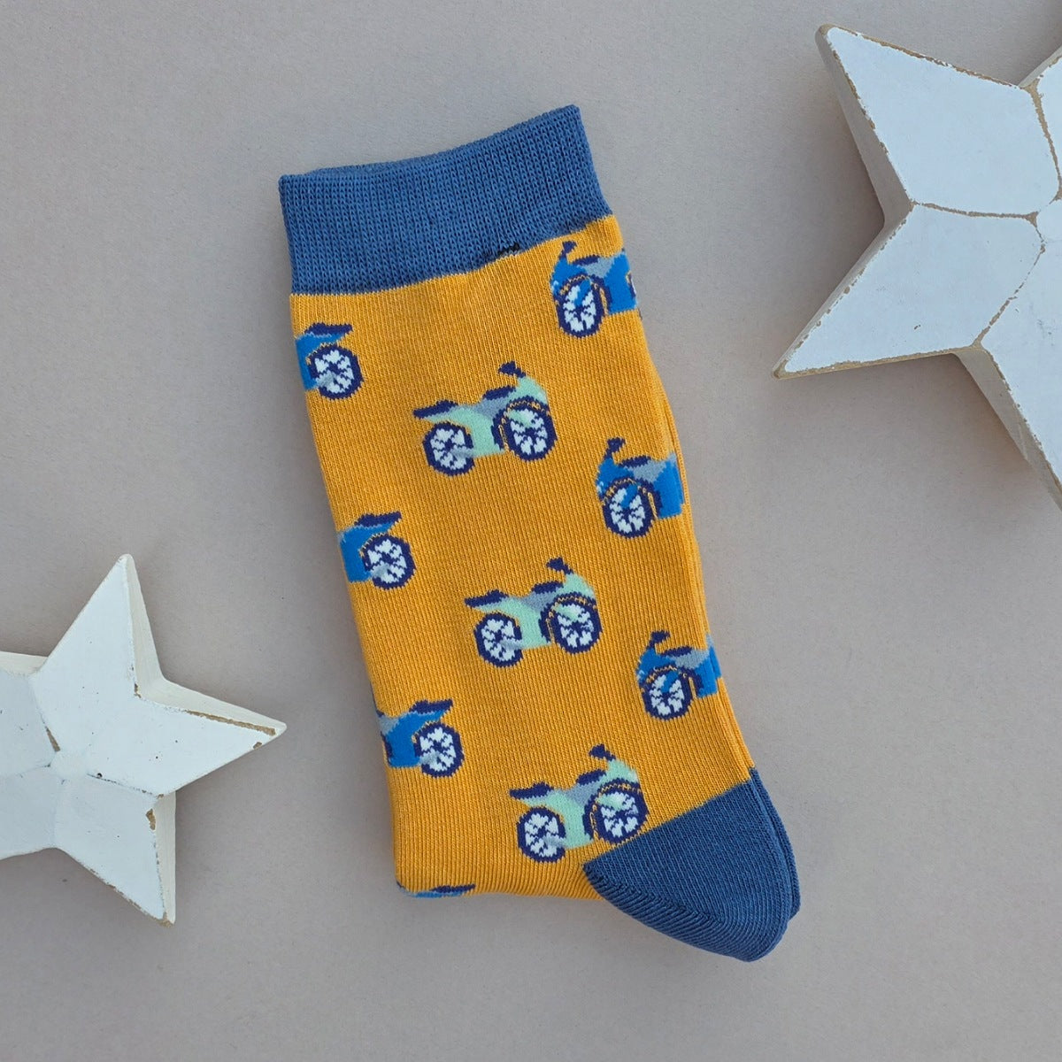 A single yellow sock with an all-over  pattern of blue motor bikes, blue ribbed cuffs and heels, styled on a light grey surface with white star props.