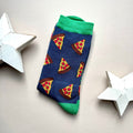 A single blue sock with an all-over  pattern of pizza slices with red pepperoni, green ribbed cuffs and heels, styled on a light grey surface with white star props