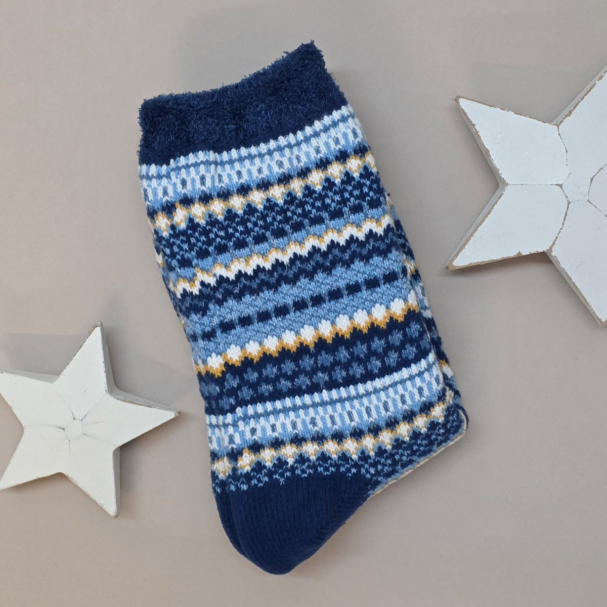 Blue and white striped sock with a detail in mustard on a grey surface with decorative stars.