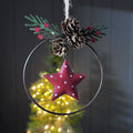 Decorative Christmas hanging ornament with a red star, pine cones, and greenery on a dark background.