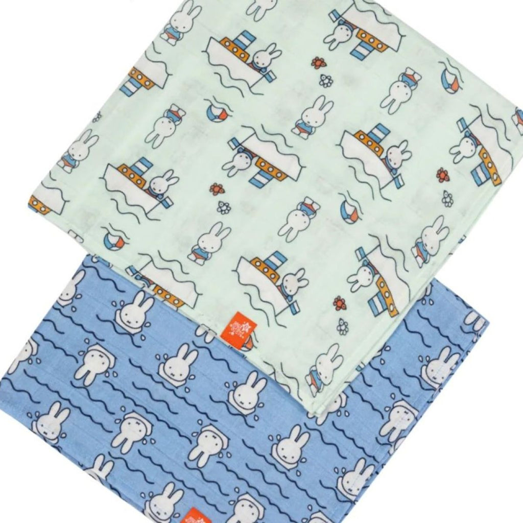 Two square baby muslin cloths with cartoon rabbit and boat prints, shown overlapping on a white background. One cloth is pale mint green and the other is light blue, both with white rabbits, blue wavy lines, and small orange accents.