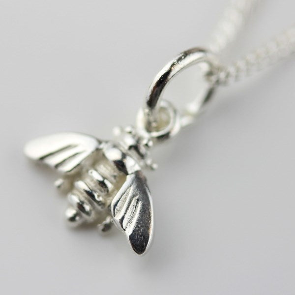 A close-up of a silver bee pendant necklace on a matching silver chain, set against a plain light gray background.