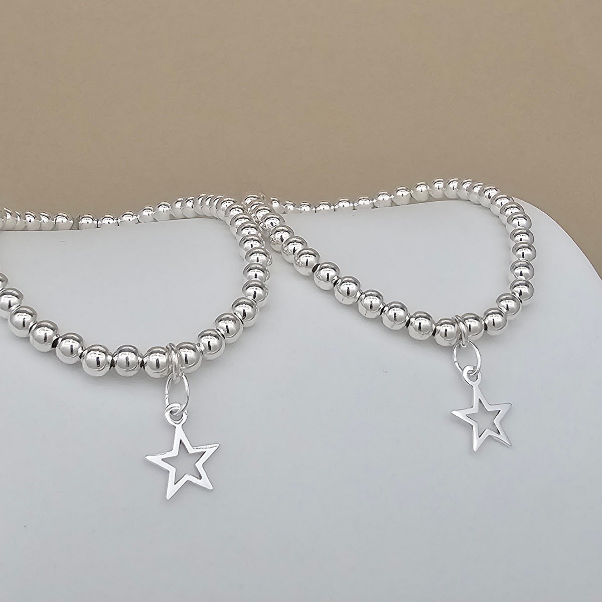 Two silver beaded bracelets with dangling star charms, displayed on a white surface against a beige background.