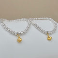 Two beaded bracelets with polished silver-toned round beads and small dangling gold heart charms, displayed on a light surface against a beige background.