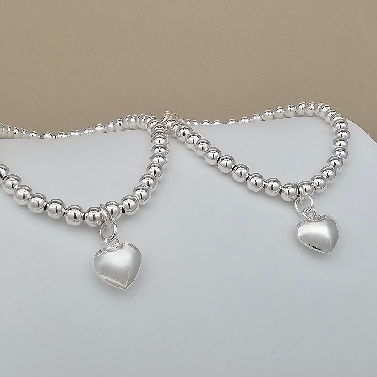 Silver beaded bracelet with heart charms on a light background