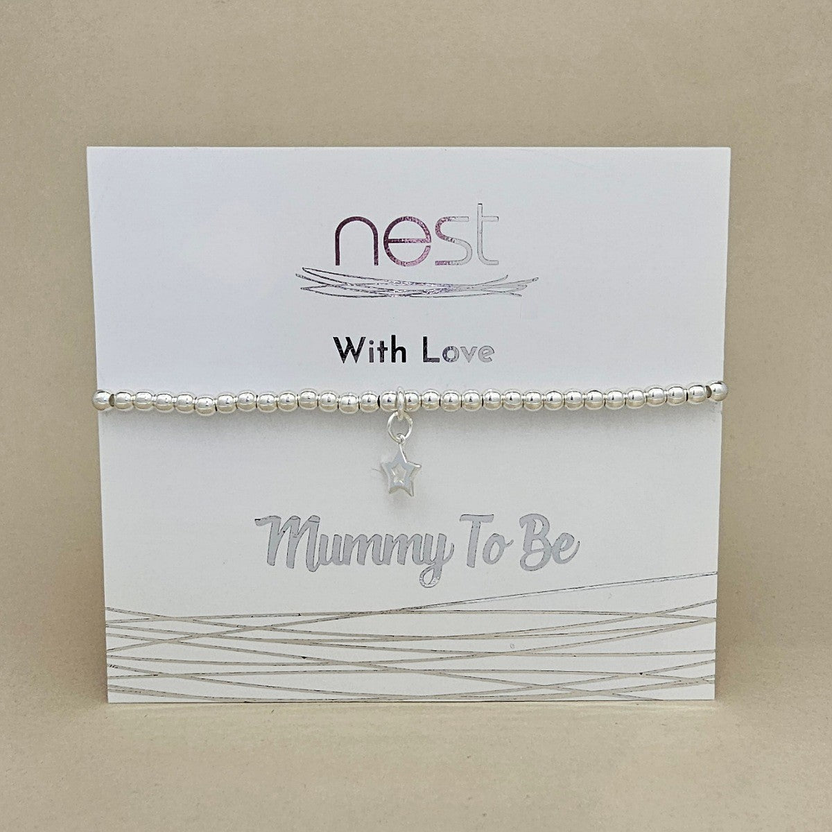 A silver beaded bracelet with a dangling star charm, presented on a white card that reads 'nest With Love Mummy To Be' against a neutral beige background.