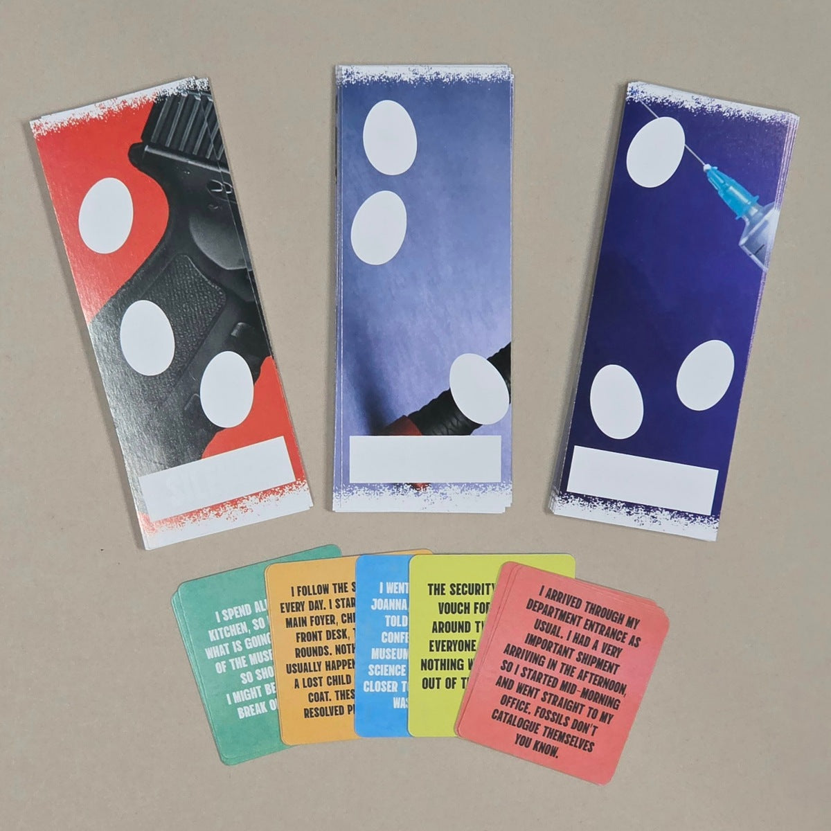 Three tall bookmark-style cards with printed illustrations are arranged on a beige surface, with six smaller text cards placed in front. The cards feature abstract red, black, white, and blue designs, plus multicolored text cards in green, orange, blue, yellow, and pink.