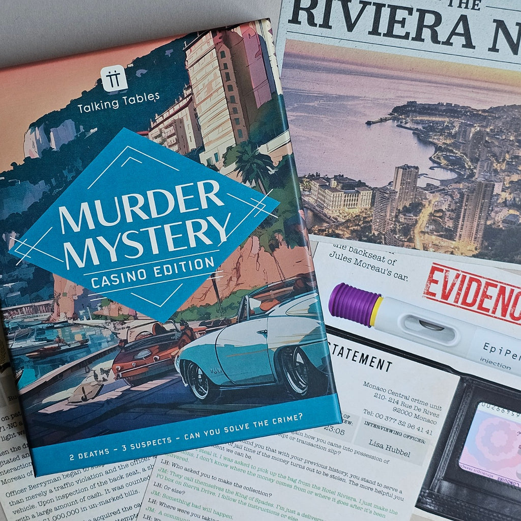 A tabletop flat-lay of a book titled "Murder Mystery Casino Edition" by Talking Tables, spread over other detective-themed printed materials including a magazine page with a casino cityscape and an evidence card.