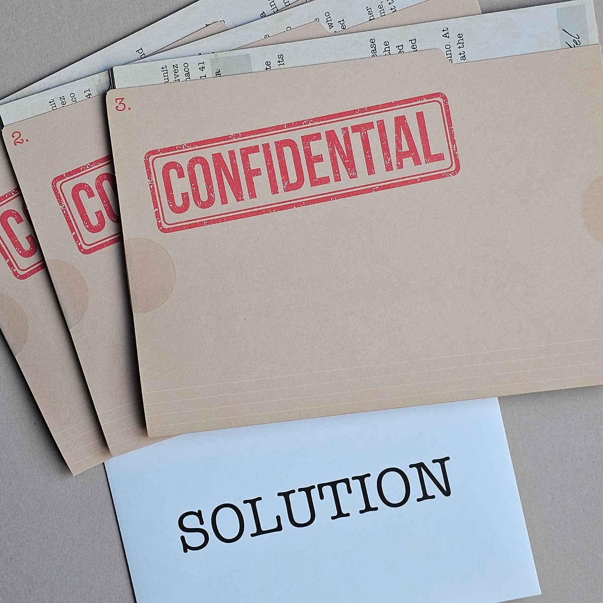 A stack of beige confidential folders stamped with 'CONFIDENTIAL' in red, with a white card labeled 'SOLUTION' in black text in front, on a neutral grey surface.