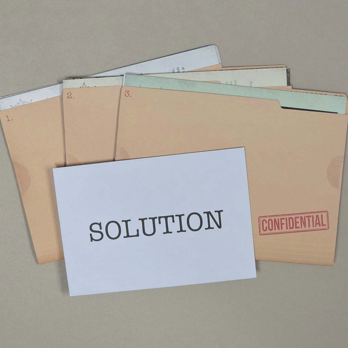 A set of beige confidential folders with numbered tabs, stacked with a white card in front that reads 'SOLUTION' and a red 'CONFIDENTIAL' stamp on the right folder, photographed on a neutral beige background.