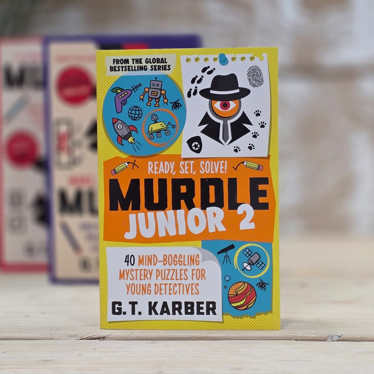 Muddle Junior 2 puzzle book by G.T. Karber on a wooden surface with a blurred background