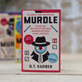 Book titled 'Murdle' by G.T. Karber, to solve 100 devilishly devious murder mystery logic puzzles on a wooden surface with blurred background