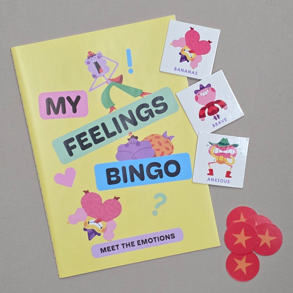 Yellow 'My Feelings Bingo' book with colorful emotion cards on a grey background