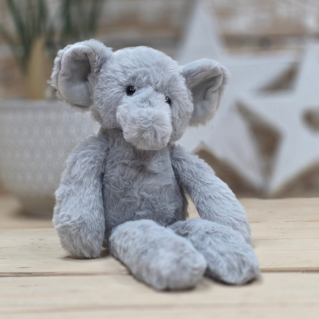 A light grey soft fuzzy plush elephant toy, with black eyes and nose, on a wooden surface with a blurred star-shaped object in the background
