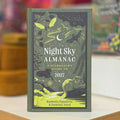 A hardcover book titled 'Night Sky Almanac: A Stargazer's Guide to 2027' by Radmila Topaloie and Dominic Ford, standing upright on a light surface with a blurred background.