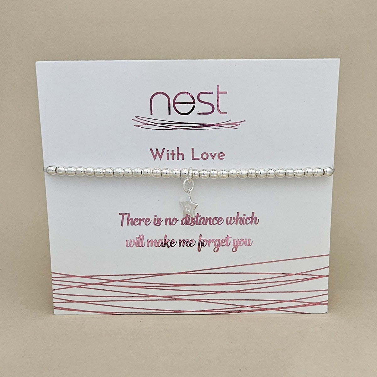 A silver beaded bracelet with a small star charm, displayed on a white card from the brand 'nest' with pink text and an inspirational quote, set against a neutral beige background.