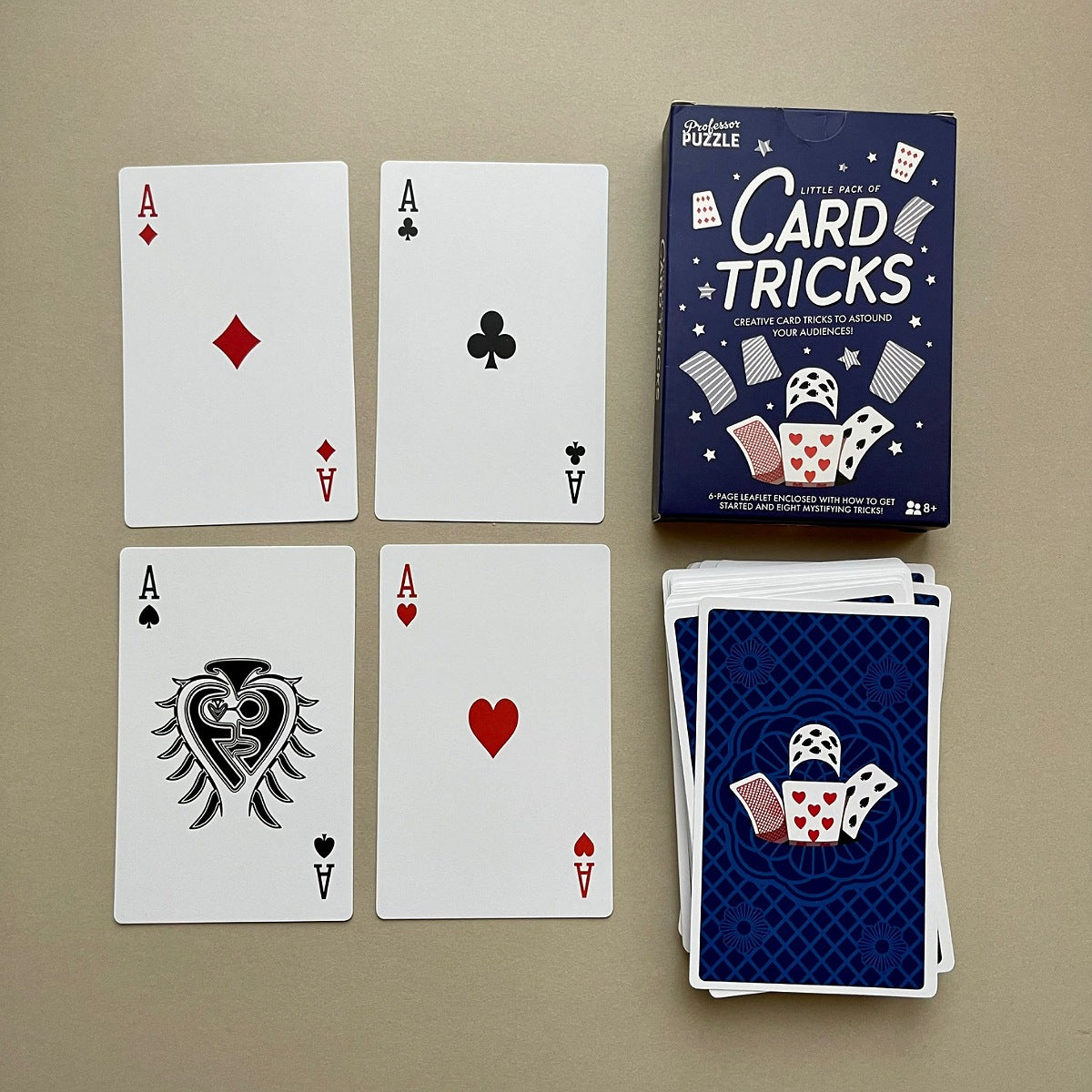 Four playing cards with different suits and a box of 'Card Tricks' on a beige background