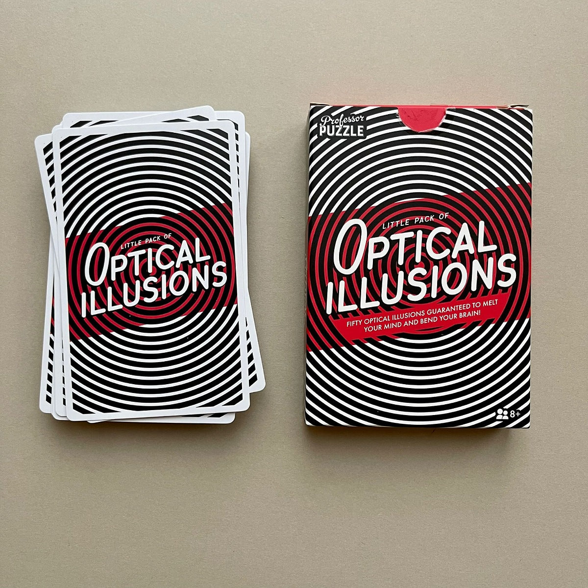 A deck of optical illusion cards and its matching retail box, both featuring a black and white spiral pattern with a red center panel and white text, displayed on a neutral beige background.